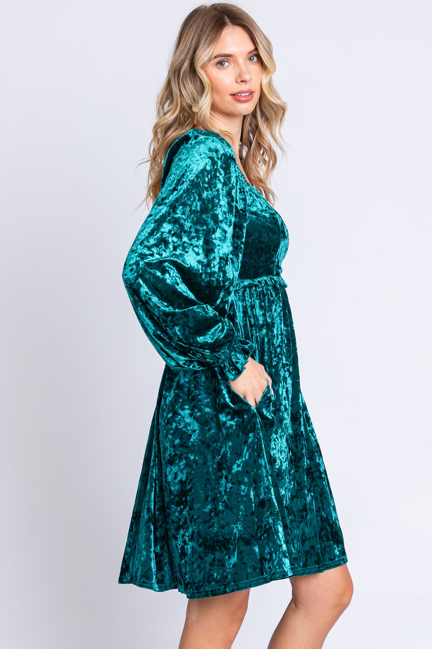 woman wearing a teal velvet long sleeve dress with a cinched waist and pockets