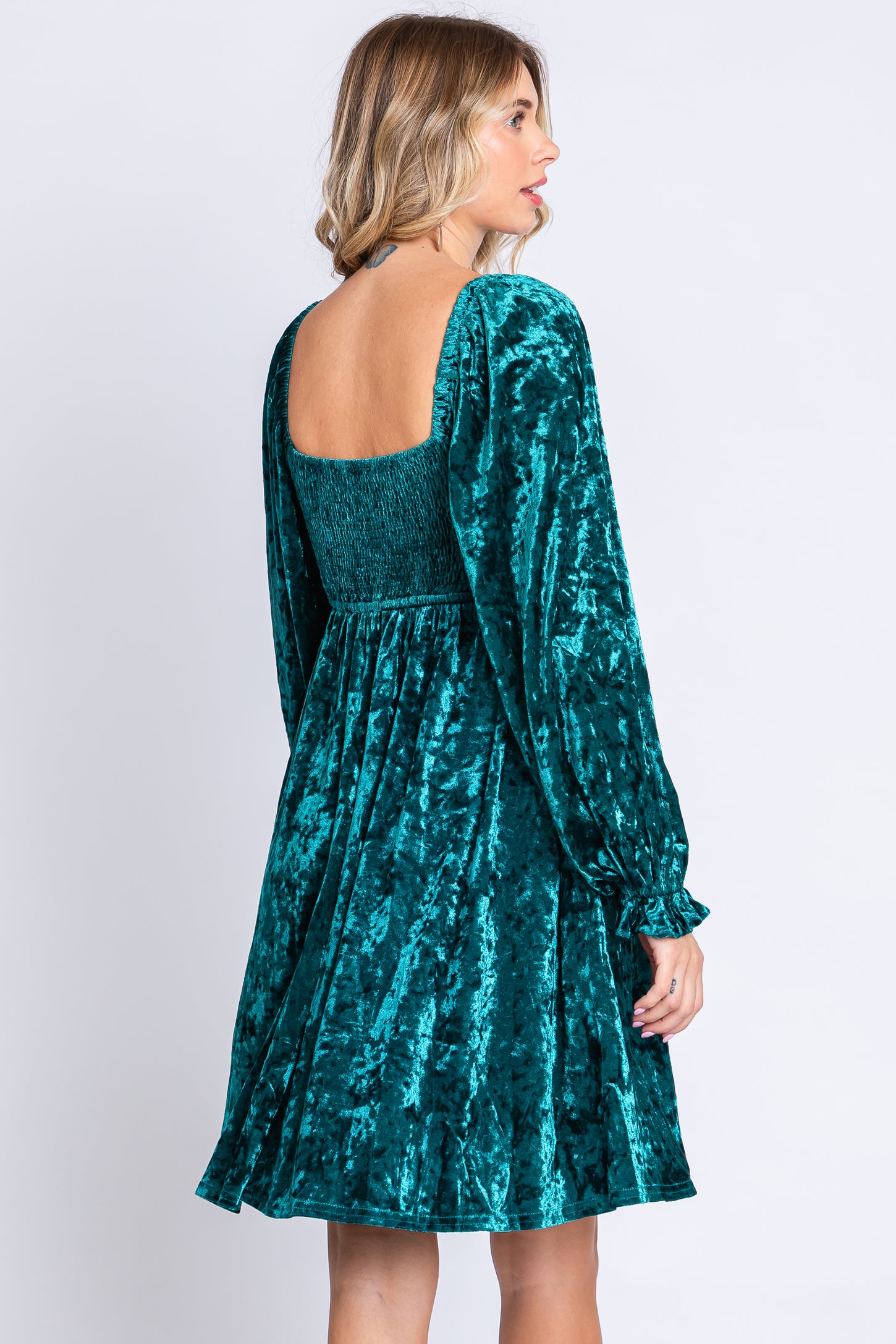 woman wearing a teal velvet long sleeve dress with a smocked bodice and flared skirt