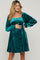 woman wearing a teal velvet maternity dress with long sleeves and a square neckline, gently holding her baby bump
