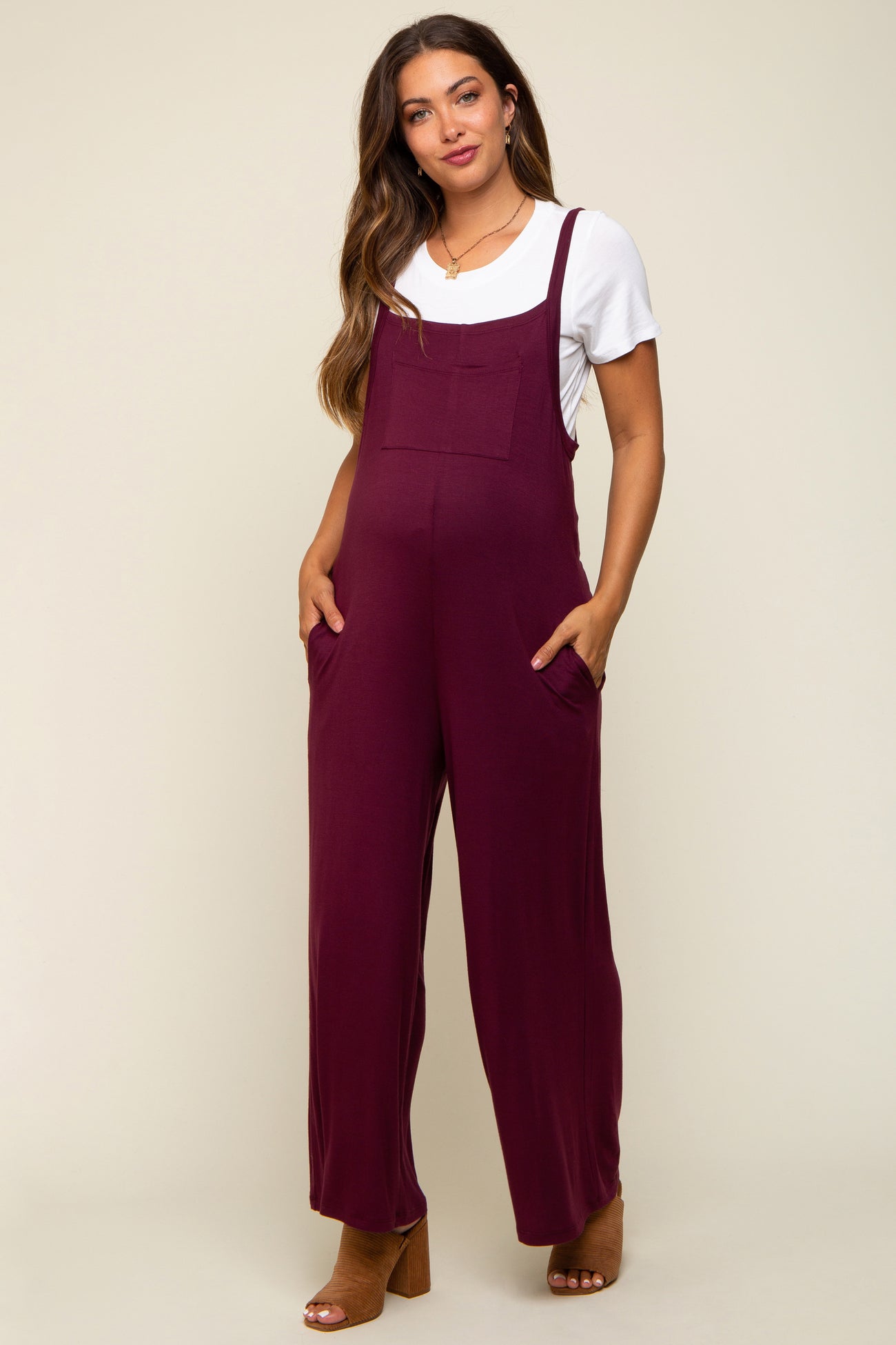 woman wearing a burgundy maternity jumper with wide legs and pockets over a white t-shirt, showcasing her baby bump