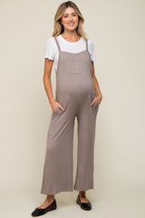 woman wearing a light brown maternity jumpsuit with pockets over a white t-shirt and showing a baby bump