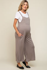 woman wearing a beige maternity jumpsuit with side pockets over a white t-shirt and showing her baby bump