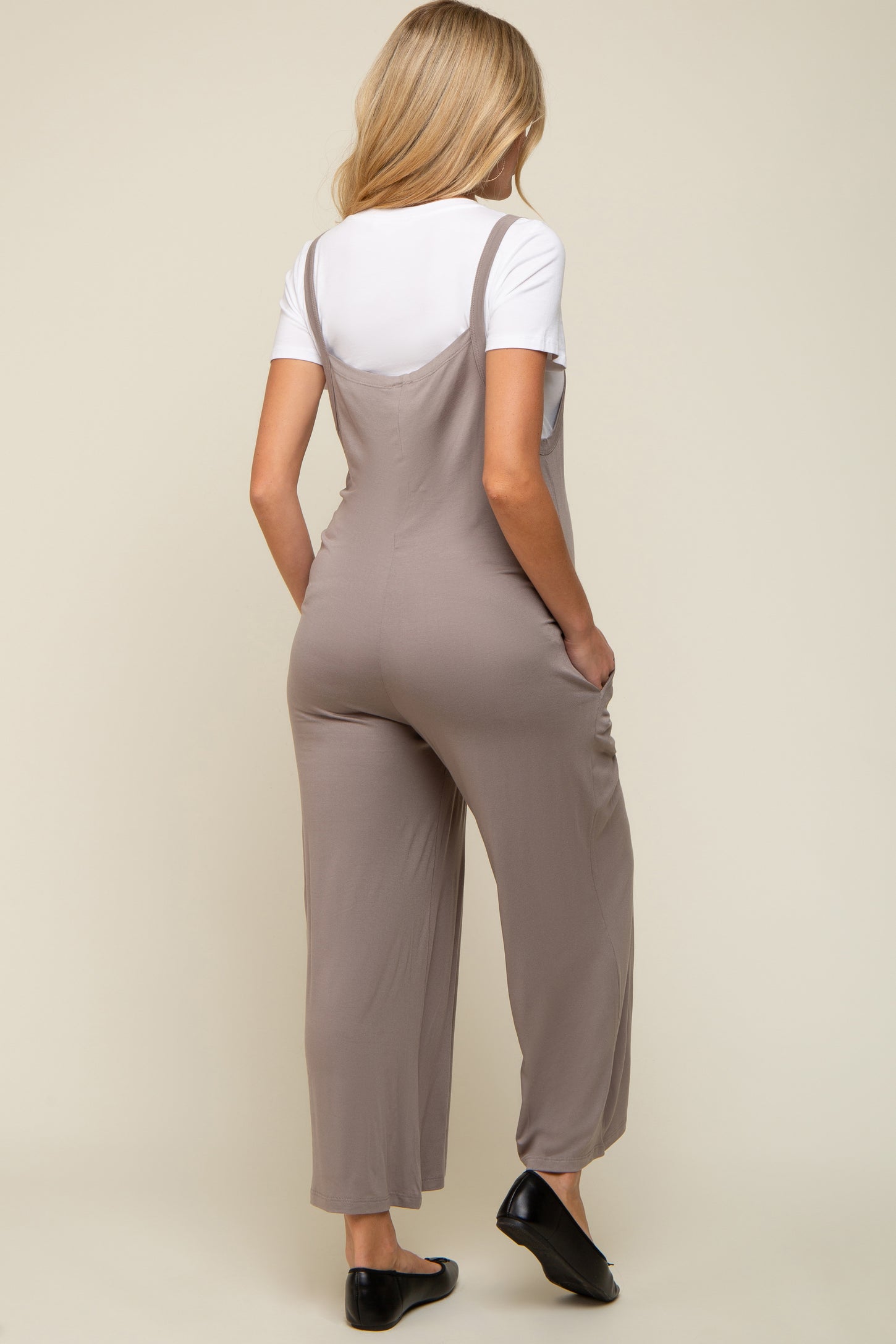 woman wearing a light gray maternity jumpsuit with adjustable straps and side pockets, viewed from the back