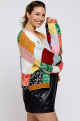 woman wearing a colorful patchwork knit maternity cardigan over a black leather skirt and smiling