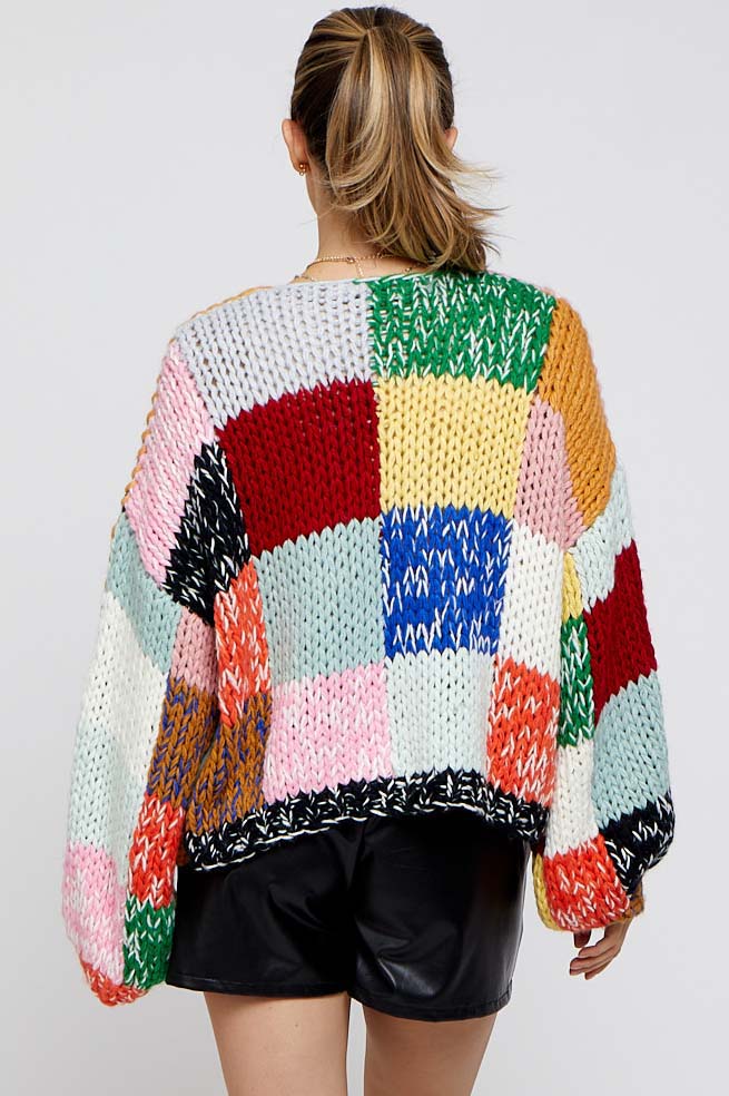 woman wearing a colorful oversized knitted maternity sweater with a patchwork design and balloon sleeves.