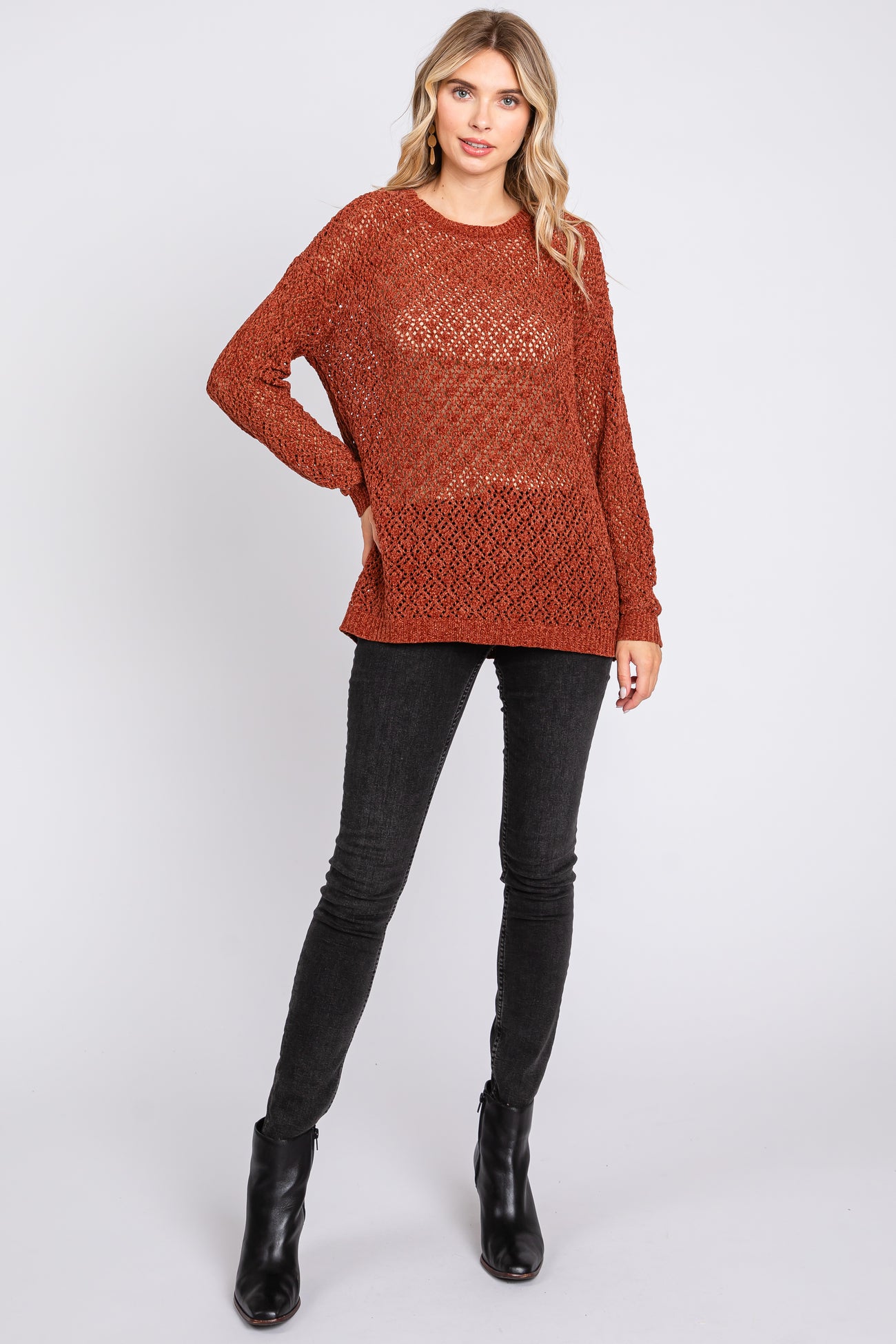 woman wearing an oversized rust-colored knit sweater and black skinny jeans, paired with black ankle boots