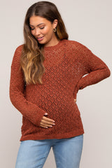 woman wearing a rust colored open knit maternity sweater and holding her baby bump