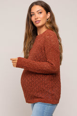 woman wearing a rust-colored open knit maternity sweater and showing her baby bump