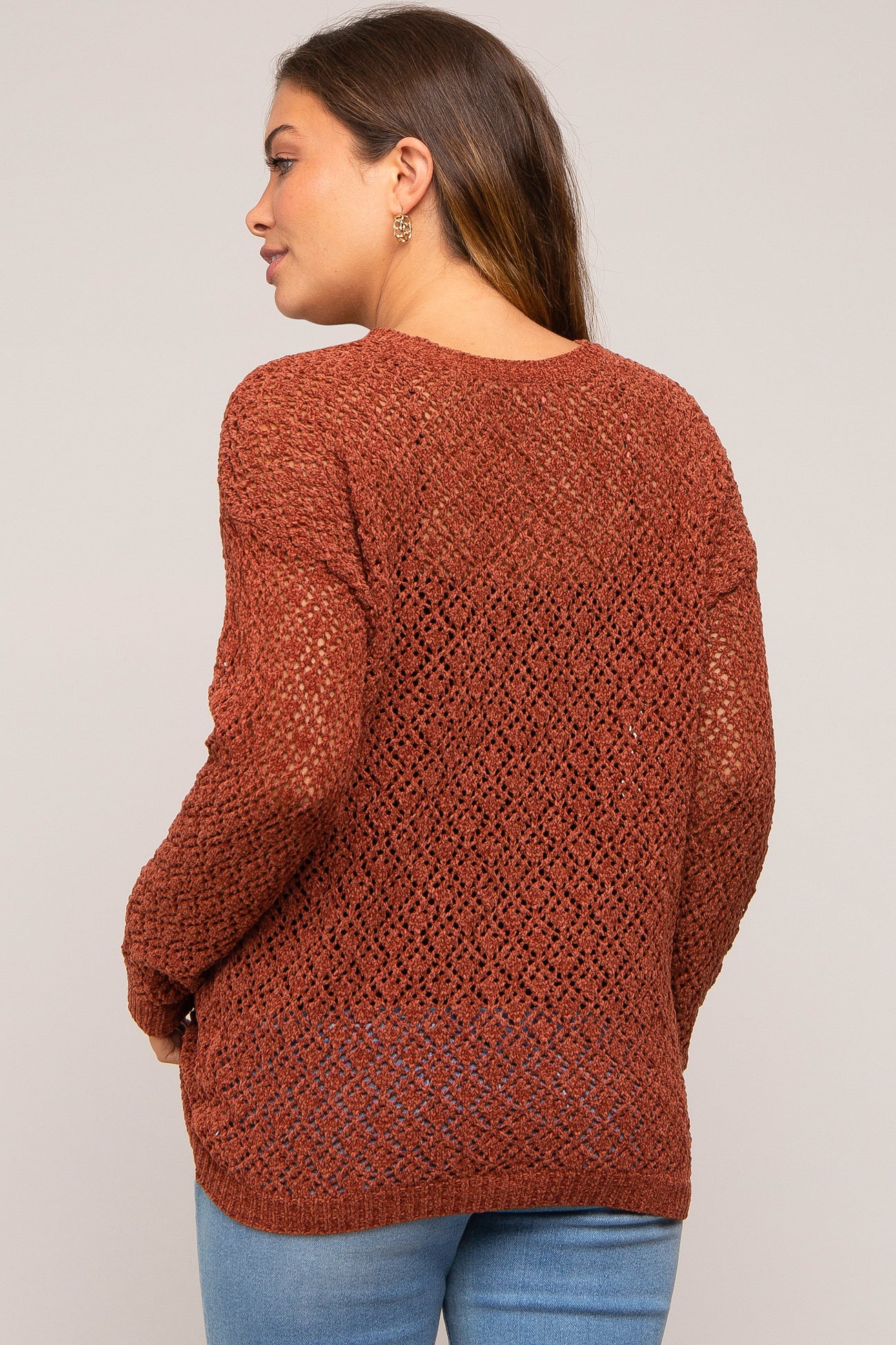 woman wearing a rust-colored open knit maternity sweater with long sleeves and a relaxed fit, viewed from the back