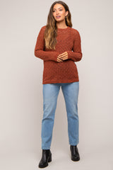woman wearing a rust-colored knitted maternity sweater paired with light blue jeans