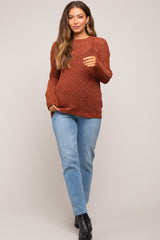 woman wearing a rust-colored maternity sweater with a textured pattern and light blue jeans, showing her baby bump
