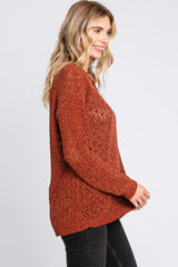 woman wearing a rust-colored knit sweater with a loose fit and open weave design, styled with black jeans