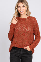 woman wearing an open knit rust colored sweater with long sleeves and a relaxed fit, paired with black jeans