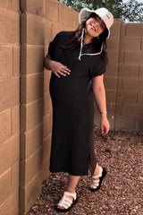 woman wearing a black striped maternity dress with a side slit, holding her baby bump and wearing a white bucket hat