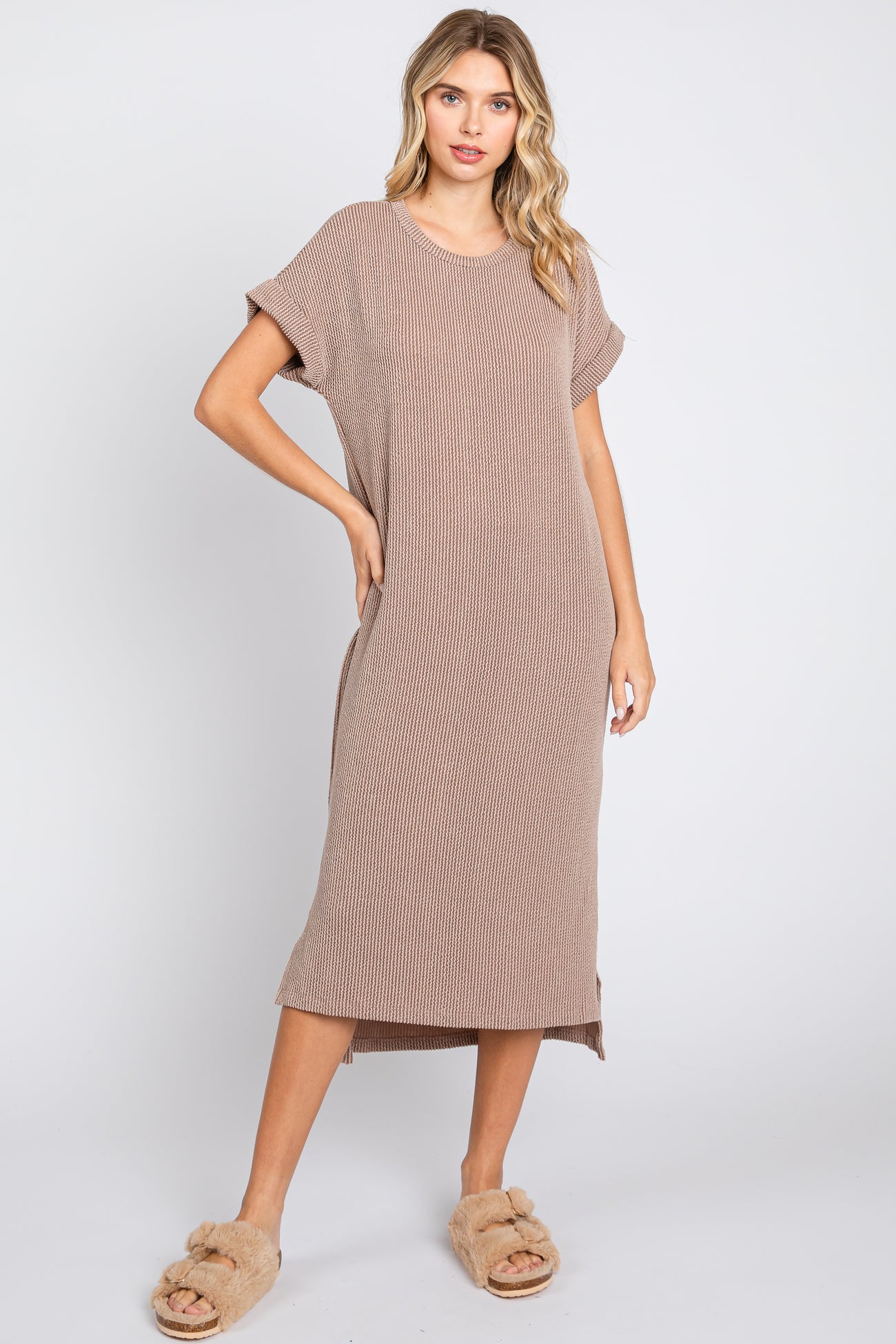 woman wearing a beige striped midi t-shirt dress with short sleeves and side slits, paired with fluffy slides