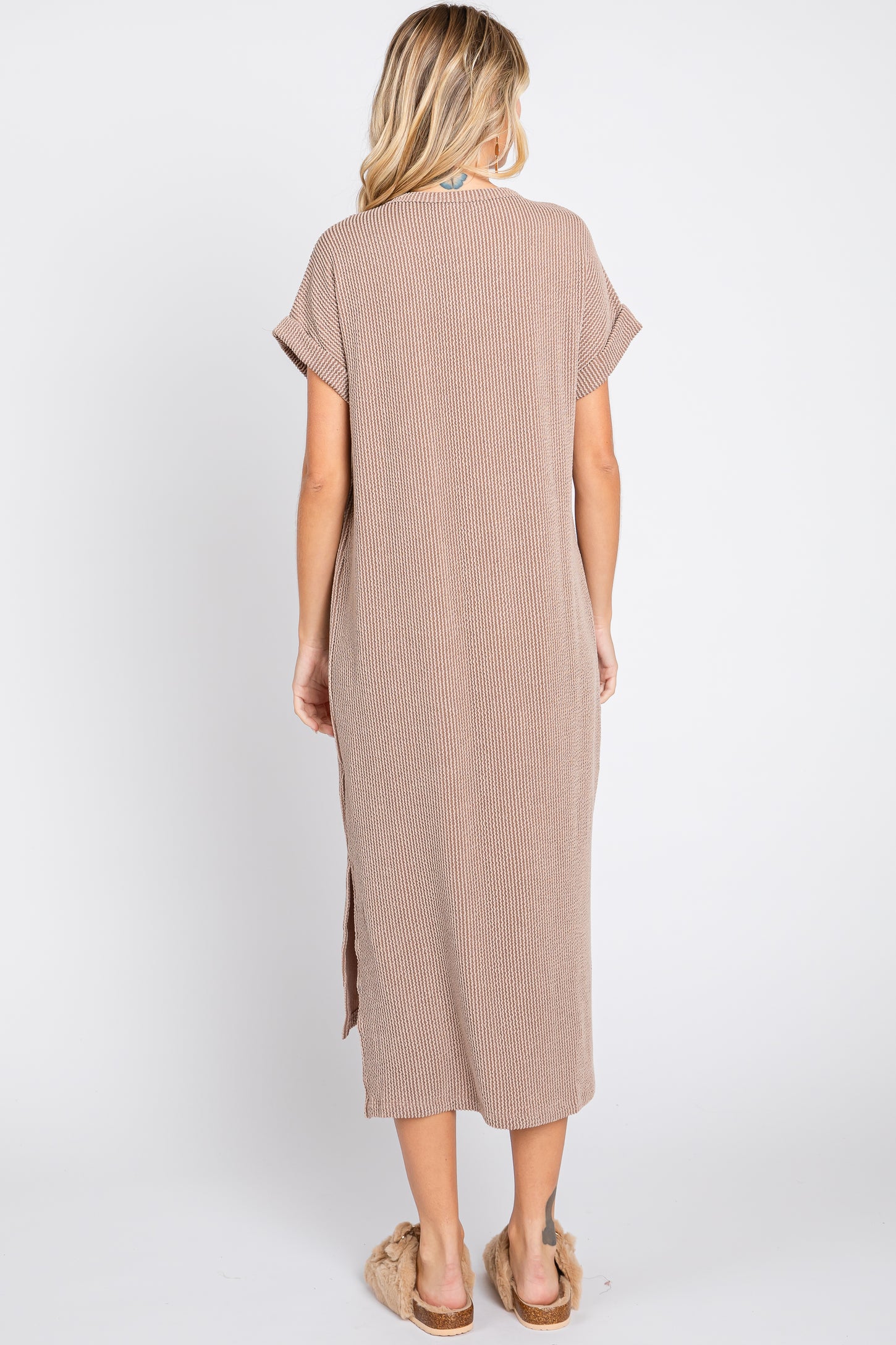 woman wearing a brown striped maxi dress with short sleeves and side slits, standing with her back to the camera