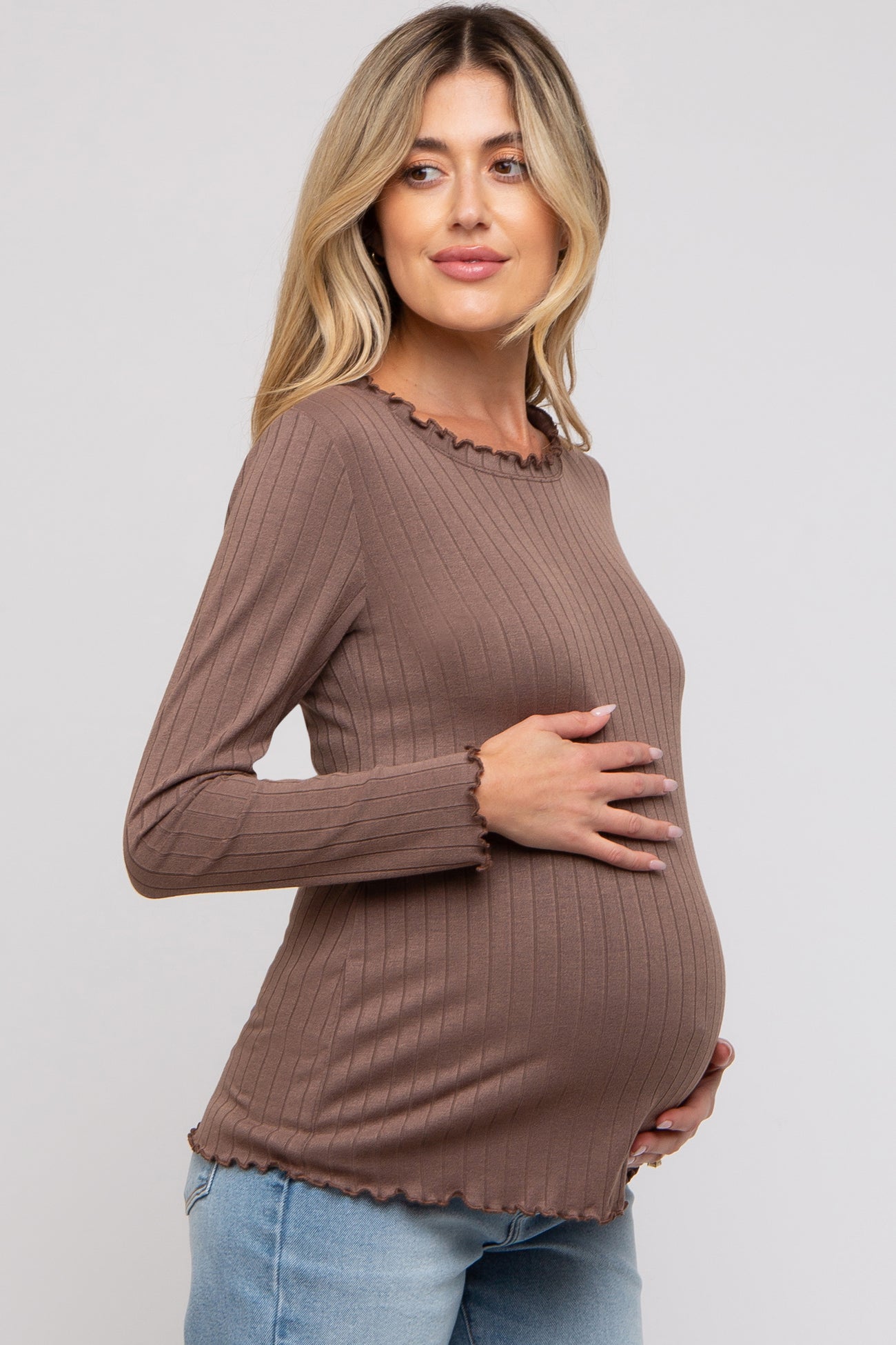 woman wearing a brown ribbed long sleeve maternity top with a scalloped neckline and holding her baby bump