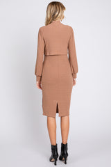 woman wearing a ribbed brown fitted dress with long sleeves and a back slit, shown from the back