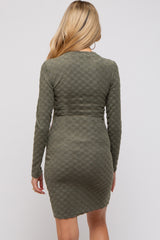 woman wearing an olive green long sleeve maternity dress with a textured checkered pattern and a fitted silhouette