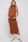 woman wearing a brown sleeveless maternity dress with a mock neck and side slit, gently cradling her baby bump