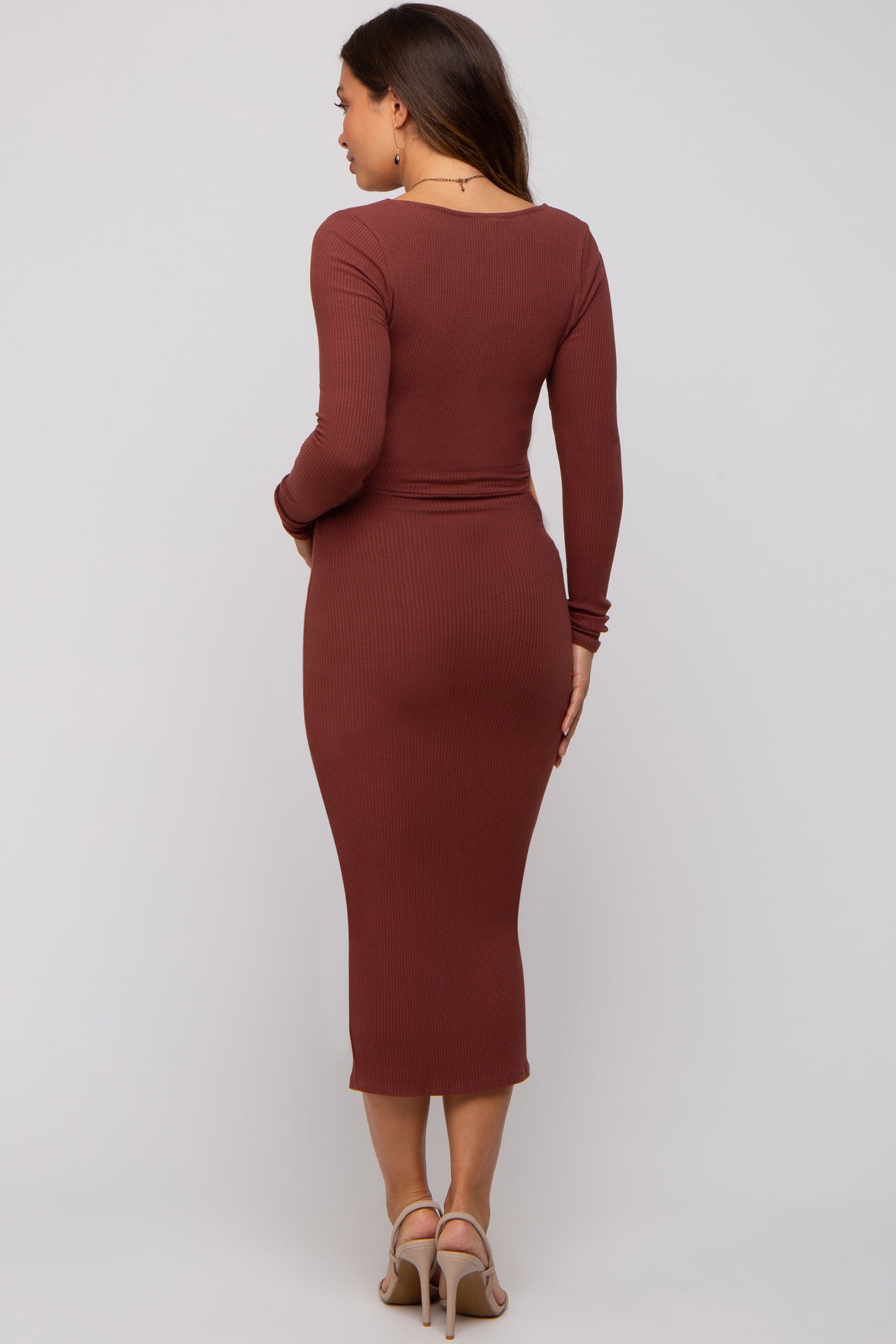 woman wearing a rust brown ribbed maternity dress with long sleeves and a form-fitting silhouette, showing her baby bump