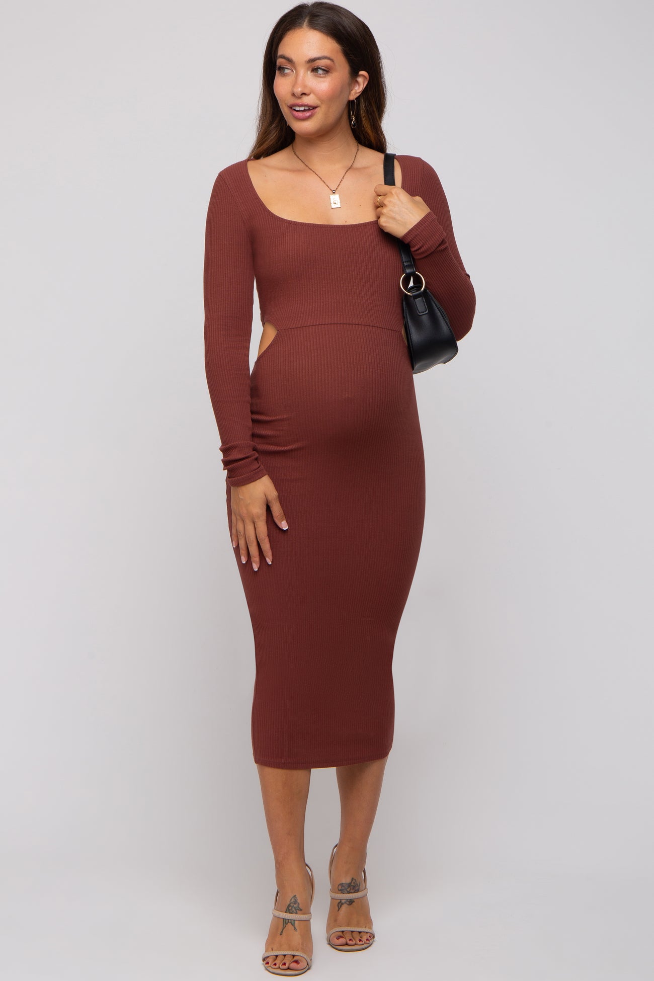 woman wearing a rust ribbed long sleeve maternity dress with cutouts and a visible baby bump, holding a black bag