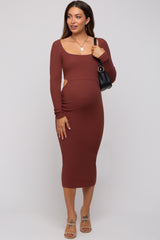 woman wearing a rust ribbed long sleeve maternity dress with cutouts and a visible baby bump, holding a black bag