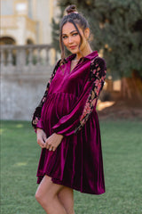 woman wearing a purple velvet maternity dress with floral long sleeves and cradling her baby bump