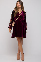 woman wearing a burgundy velvet maternity dress with floral embroidered sleeves and a baby bump, carrying a small bag