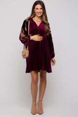 woman wearing a burgundy velvet maternity dress with floral sleeves and holding her baby bump