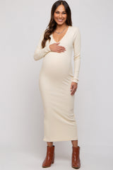 woman wearing a beige ribbed maternity dress with long sleeves and a v-neck, holding her baby bump