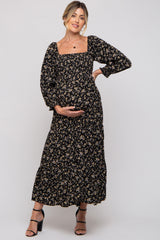 woman wearing a black floral maternity maxi dress with long puff sleeves and holding her baby bump