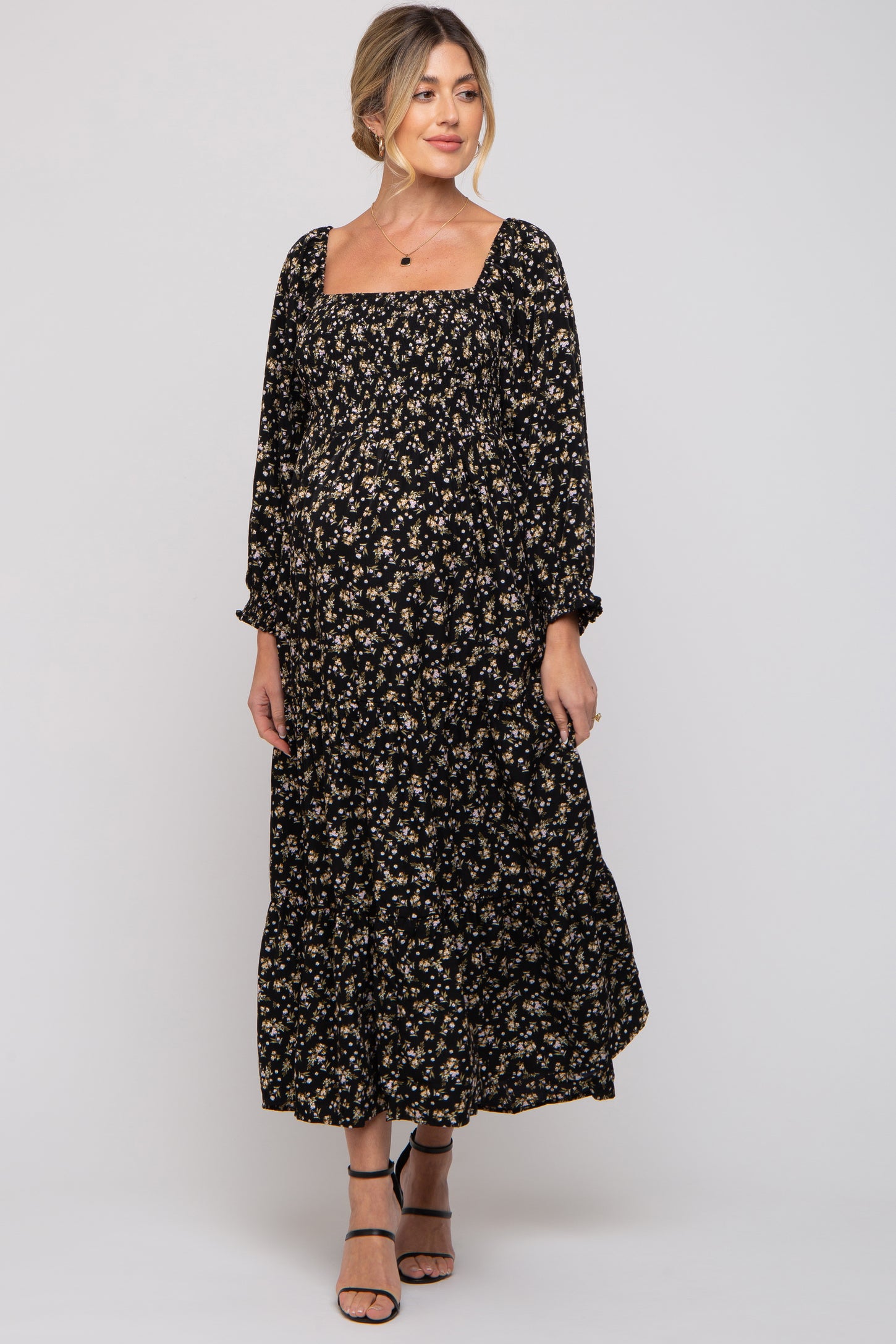 woman wearing a black floral maternity dress with long sleeves and a square neckline, featuring a flowing skirt and visible baby bump