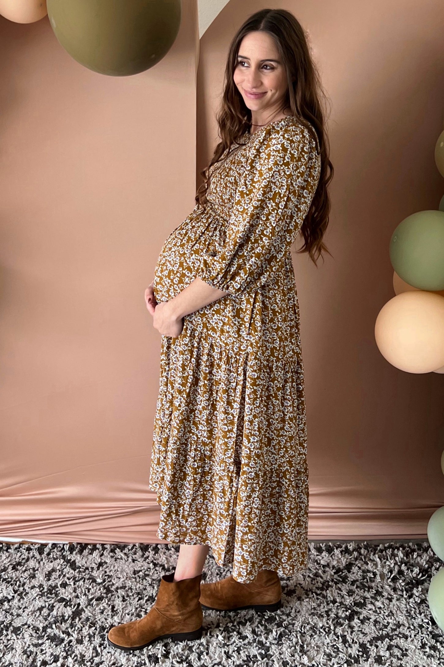 woman wearing a long sleeve mustard floral maternity dress and showcasing her baby bump