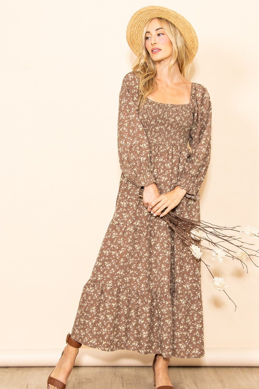 woman wearing a brown floral maxi dress with long sleeves and a smocked bodice, holding dried flowers and wearing a straw hat