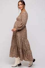 woman wearing a brown floral maternity maxi dress with a tiered skirt and long sleeves, showing her baby bump