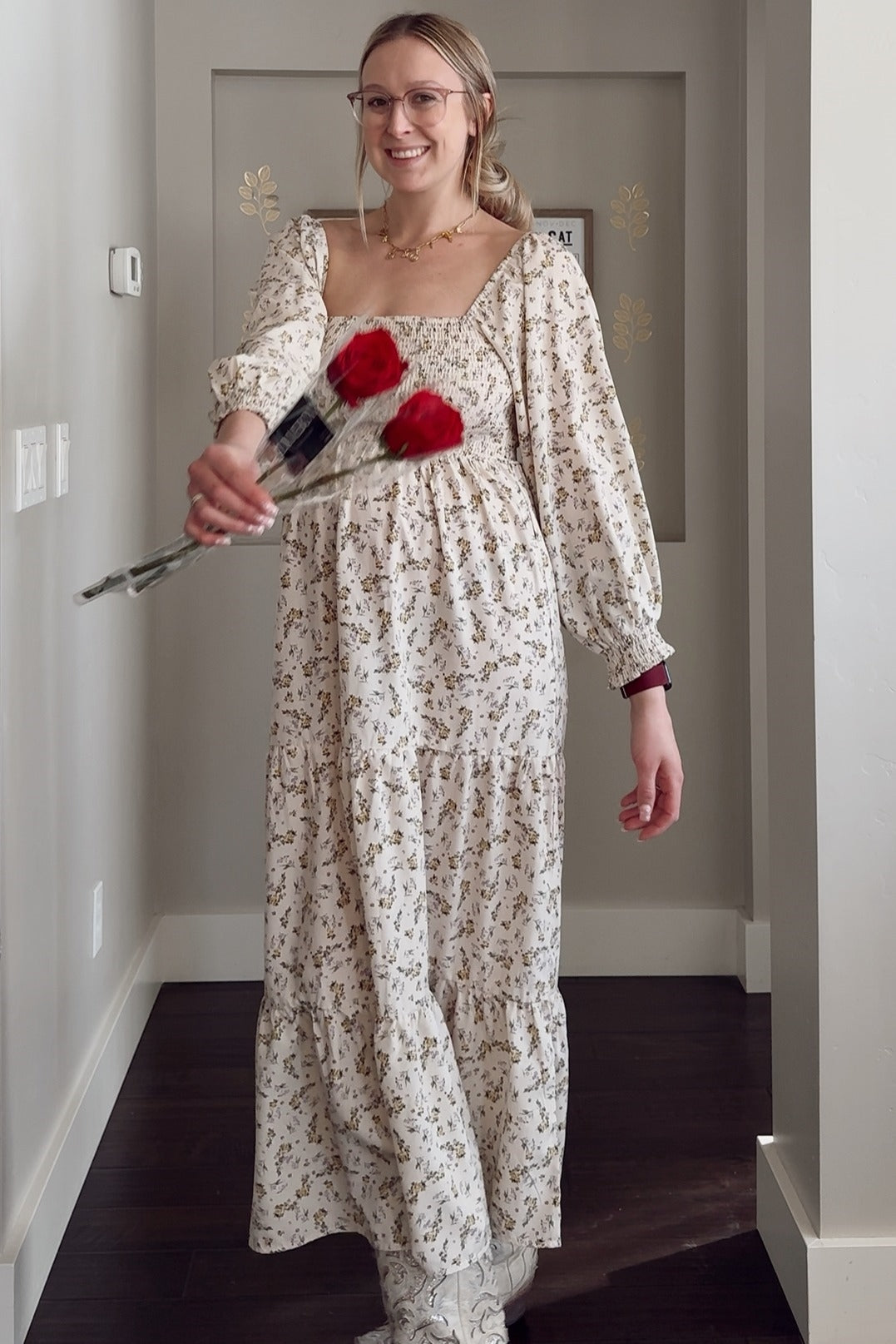 woman wearing a cream floral maternity maxi dress with puff sleeves and holding three red roses, showing her baby bump