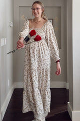woman wearing a cream floral maternity maxi dress with puff sleeves and holding three red roses, showing her baby bump