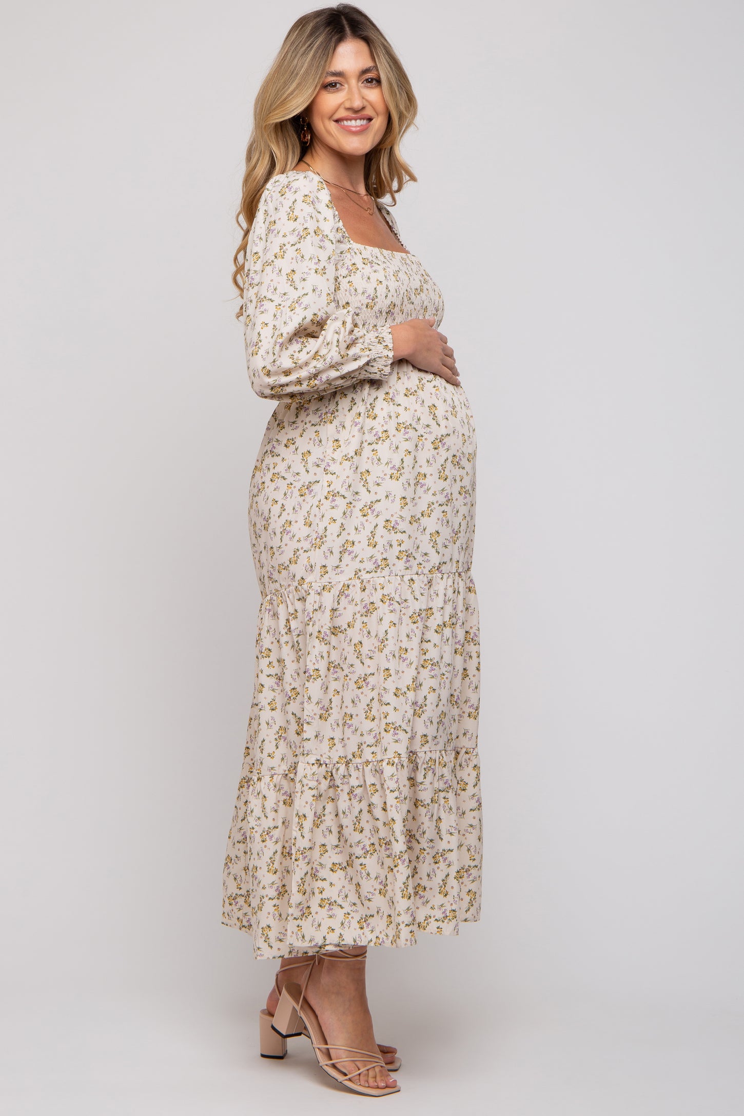 woman wearing a floral long sleeve maternity dress with a tiered skirt and holding her baby bump