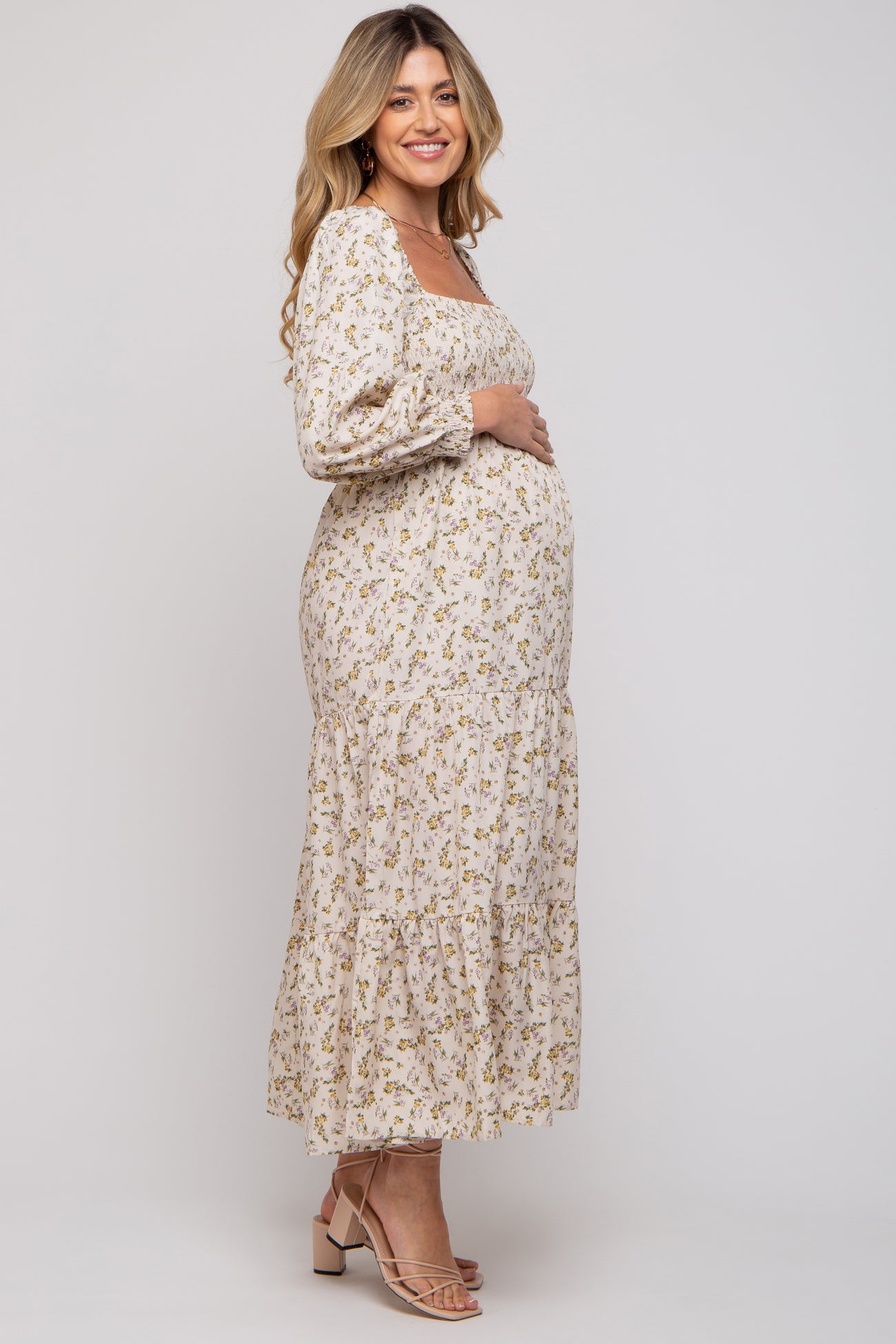 woman wearing a floral long sleeve maternity dress with a tiered skirt and holding her baby bump