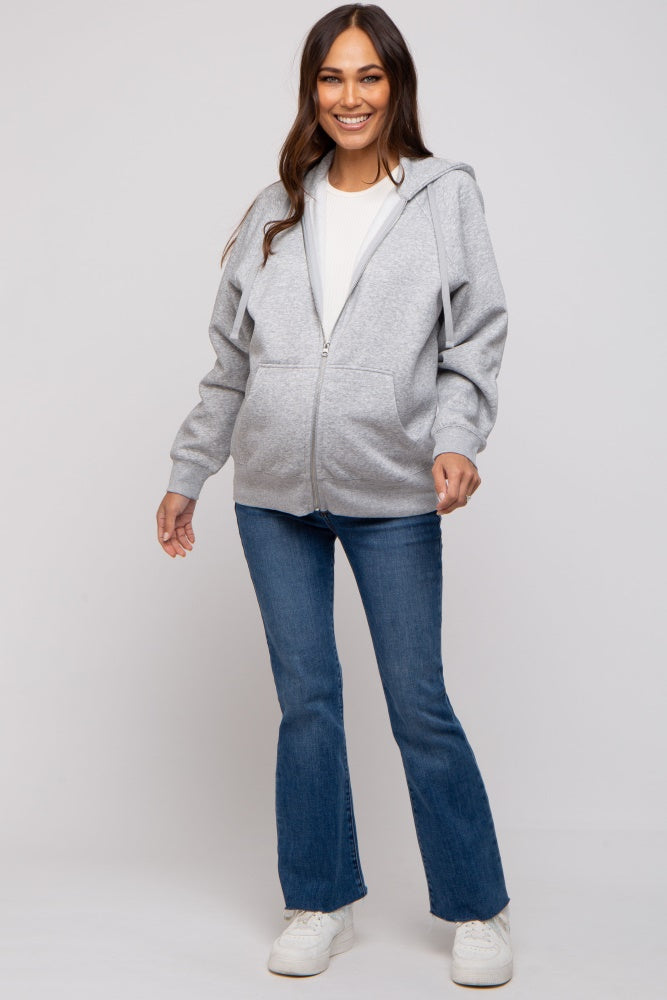 woman wearing a gray zip-up hoodie and flared jeans, styled for maternity wear with a baby bump visible