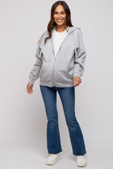 woman wearing a gray zip-up hoodie and flared jeans, styled for maternity wear with a baby bump visible