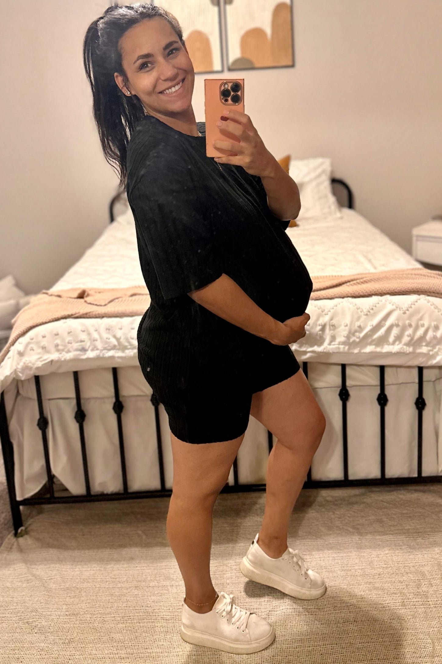 woman wearing a black maternity lounge set and holding her baby bump in front of a mirror