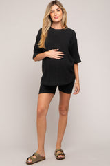 woman wearing a black ribbed maternity top and black shorts, holding her baby bump