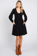 woman wearing a black long sleeve swing dress with a v-neck and pockets, paired with brown ankle boots
