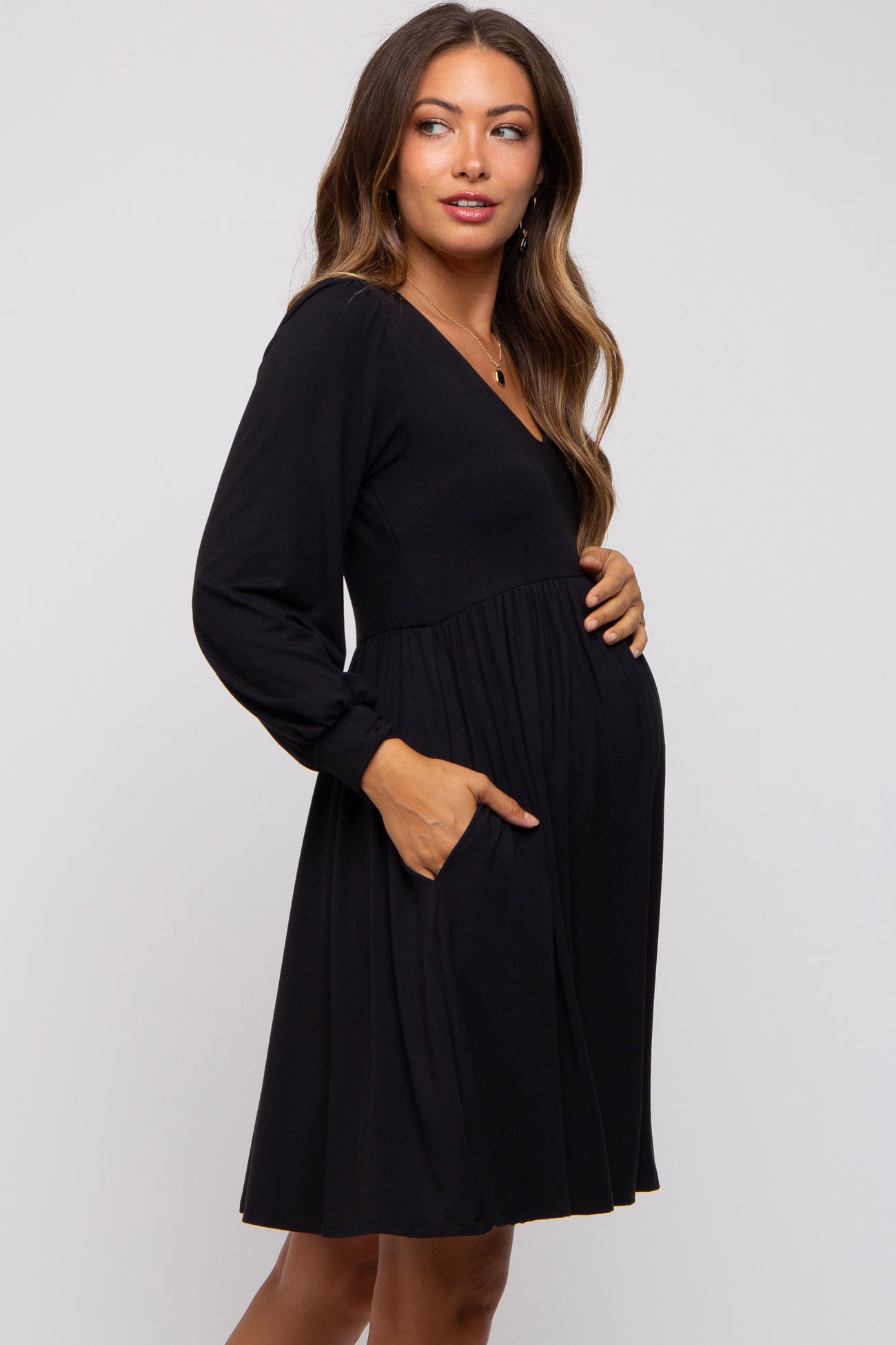 woman wearing a black long sleeve maternity dress with pockets and a visible baby bump