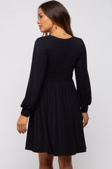 woman wearing a black long sleeve maternity dress with a fitted bodice and flared skirt