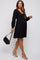 woman wearing a black long sleeve maternity dress with a v-neck and holding a small black handbag, showing her baby bump