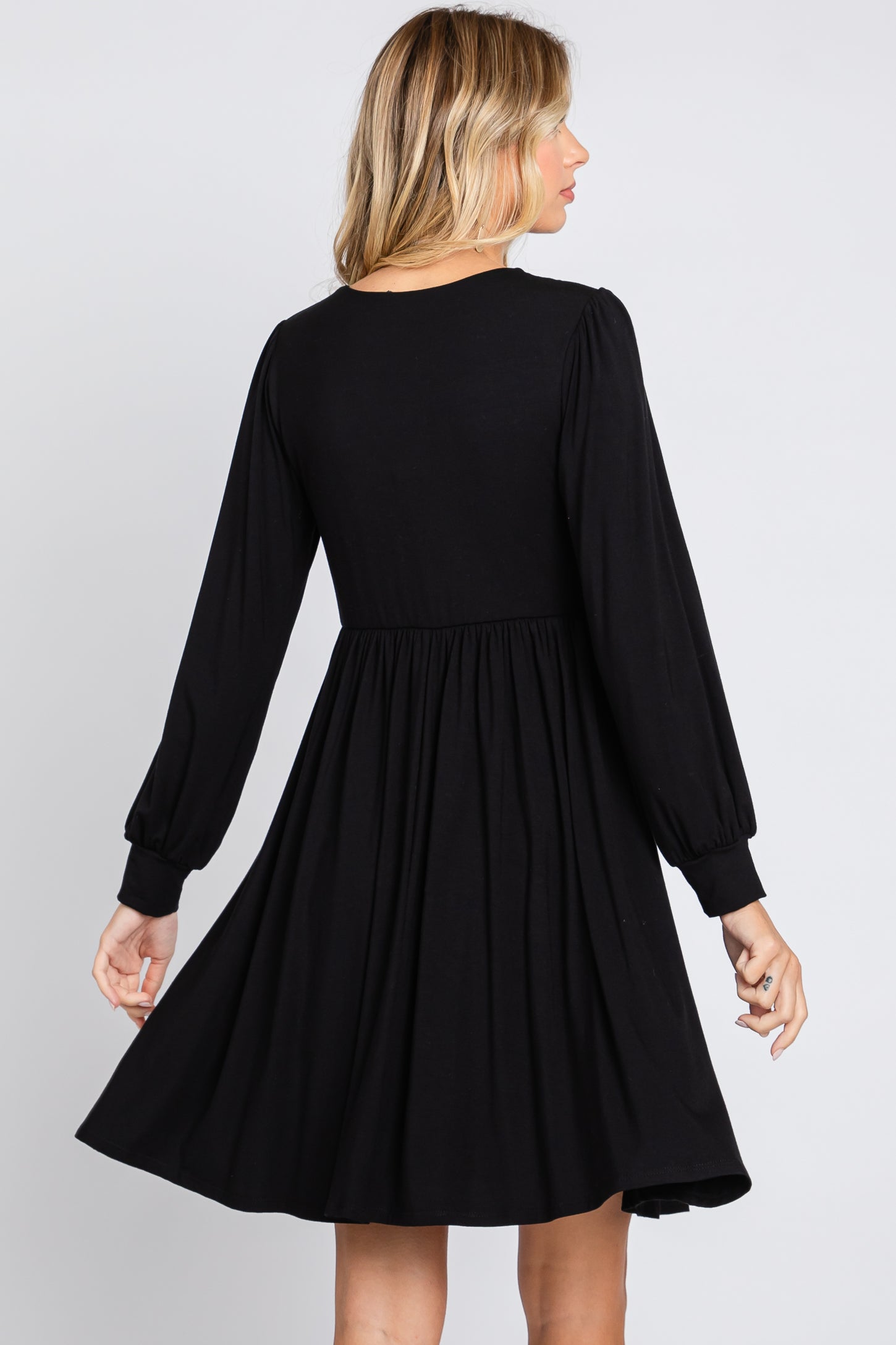 woman wearing a black long sleeve dress with a fitted bodice and flared skirt, viewed from the back