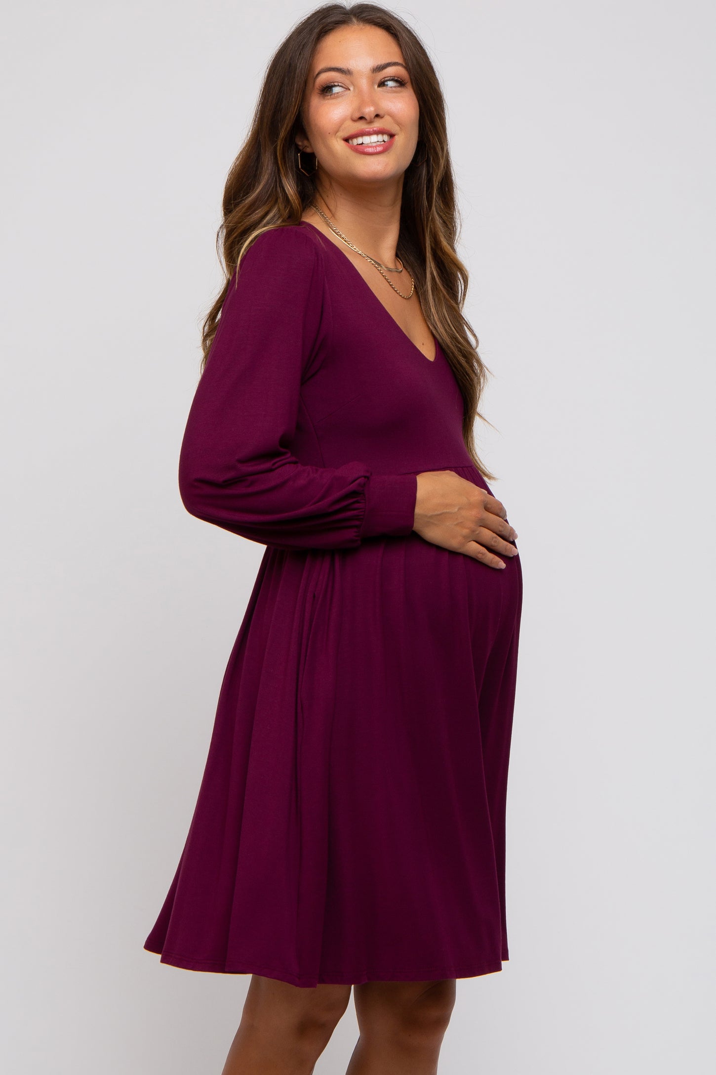 woman wearing a burgundy maternity dress with a v-neck and long sleeves, gently holding her baby bump